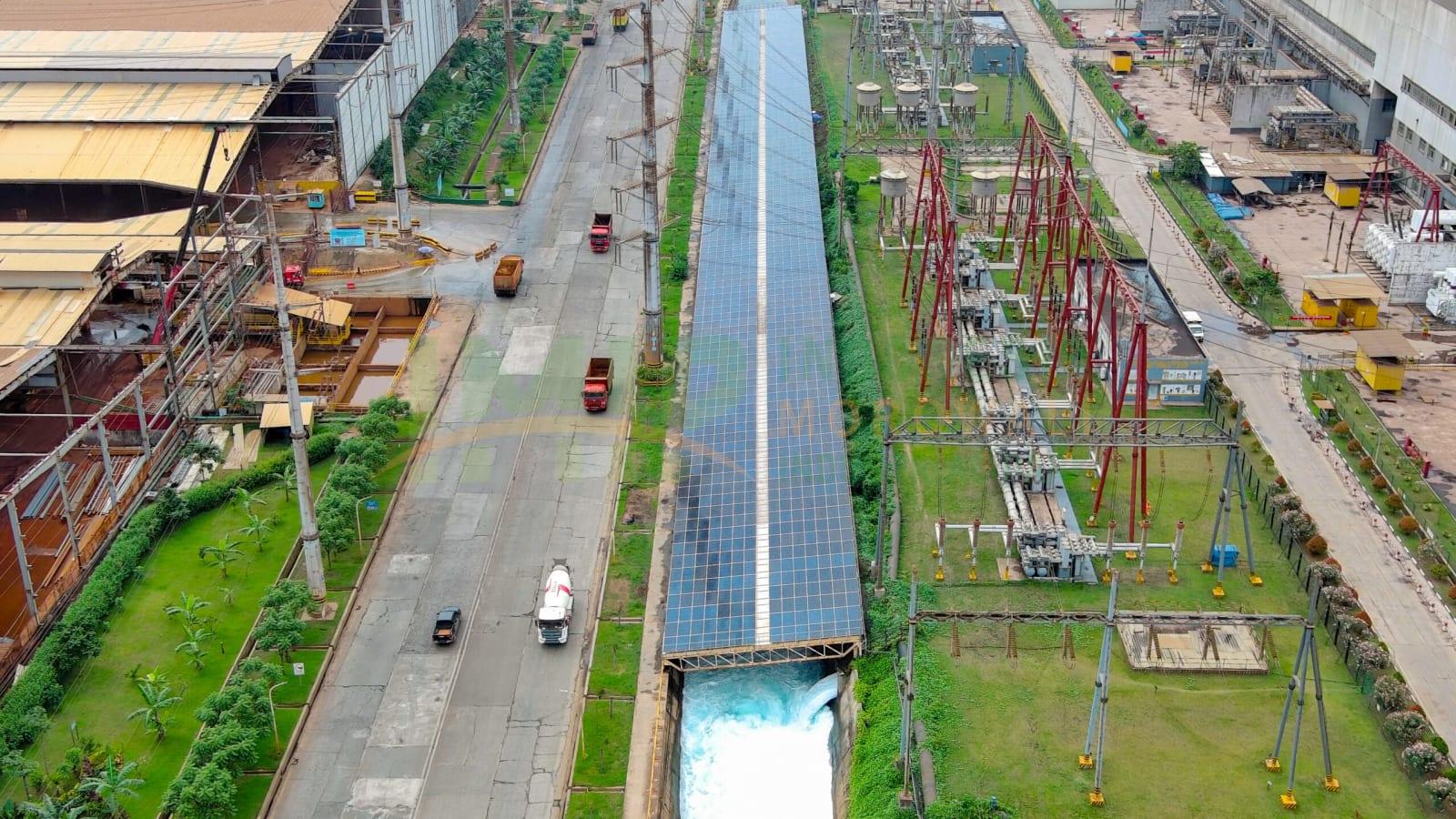Aerial view of solar panels covering large factory roofs and a canal inside the Morowali industrial park, with smelter buildings and hills in the background
