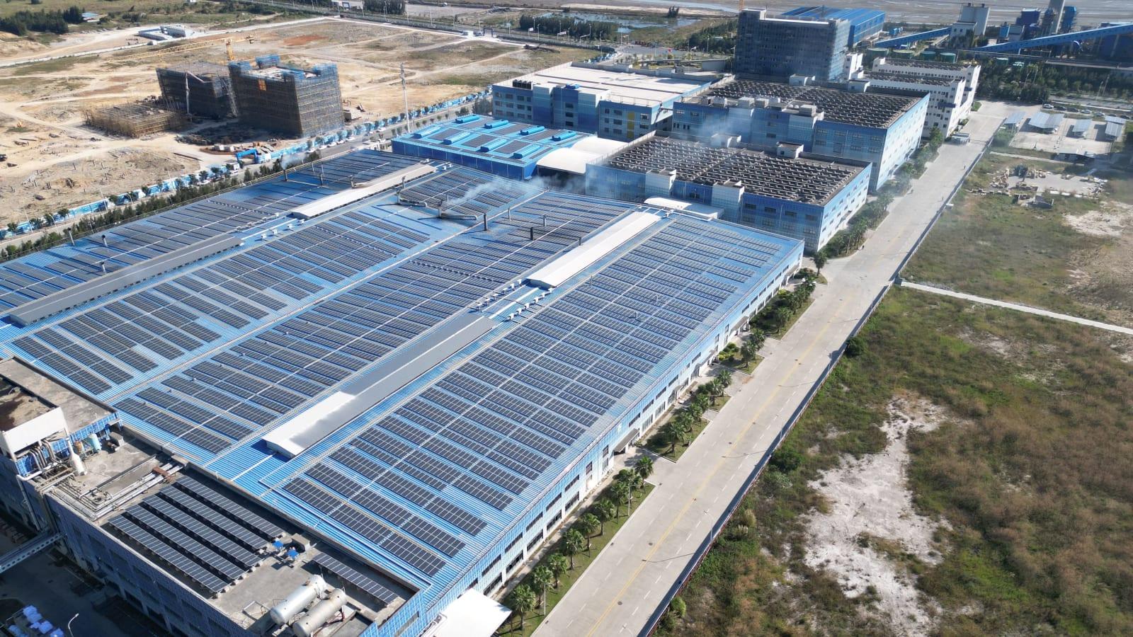 Rooftop solar panels across factory buildings in an Indonesian industrial estate, with a high voltage substation and transmission towers in the background