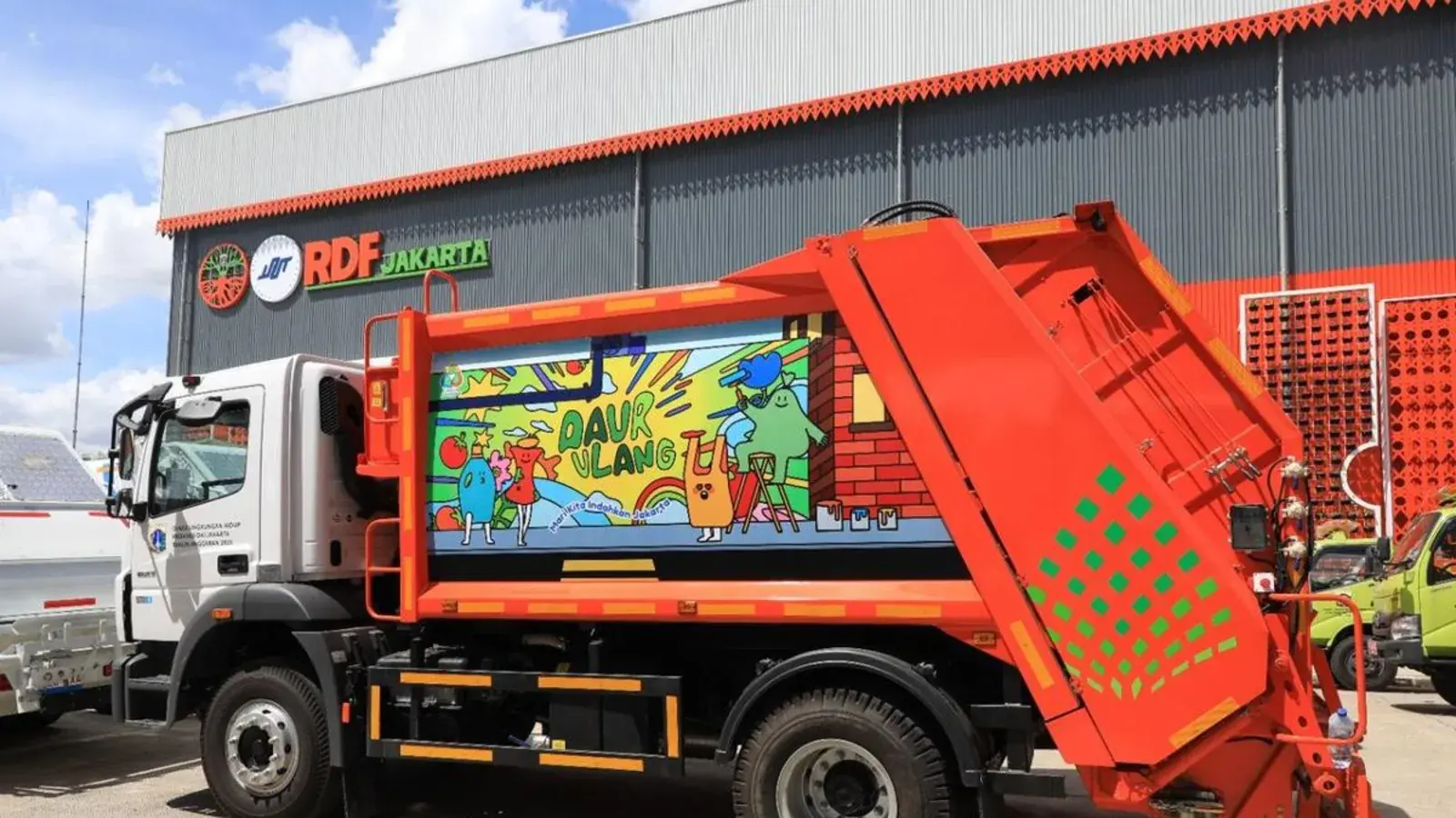 A row of refurbished orange garbage compactor trucks parked in a Jakarta municipal depot, ready for handover, with a Bogor city official and a Jakarta official inspecting one of the rear compactor units