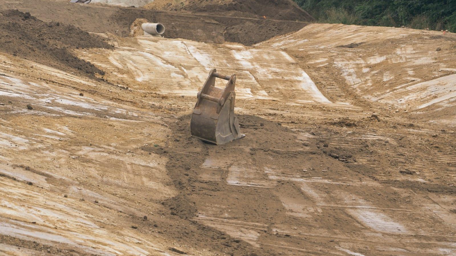 Revegetated post-mining terraces on a hillside with young trees established, a surveyor with GPS equipment measuring plot boundaries in the foreground